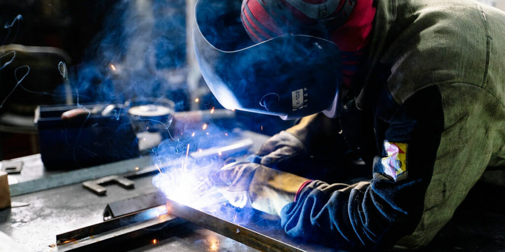 A metalworker welds steel at a workbench.